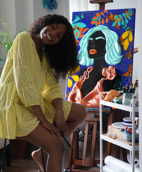 Woman sitting on a chair with a colorful painting of a woman's face in the background.